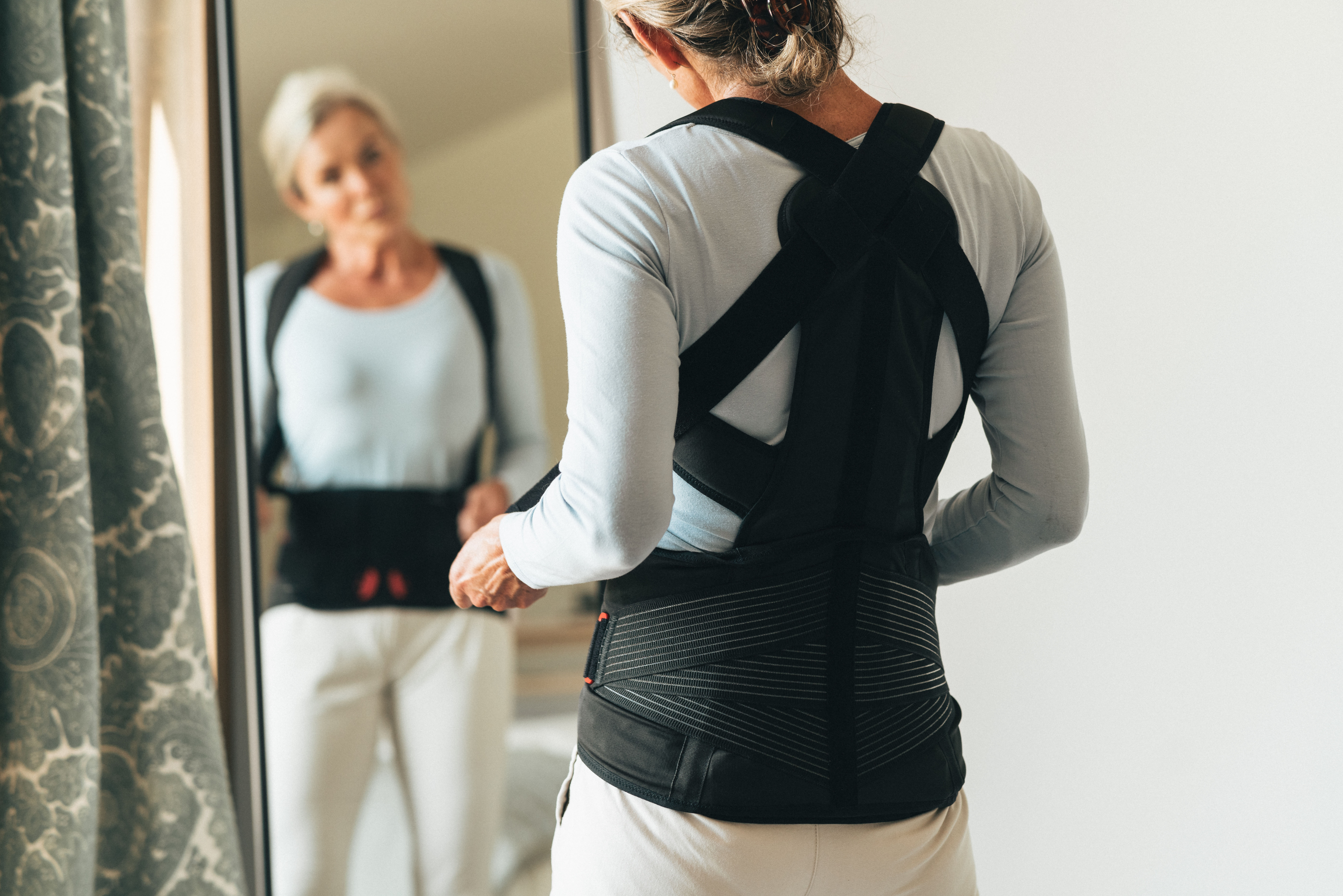 Imagebild DONJOY® OsteoStrap Frau vor dem Spiegel, Rückenorthese zur aktiven Entlastung der LWS/BWS